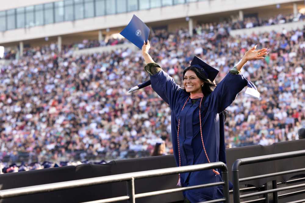 A college graduate smiles and waves at a ceremony.