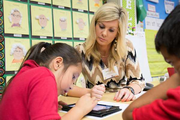 A teacher works with students wearing red shirts. 