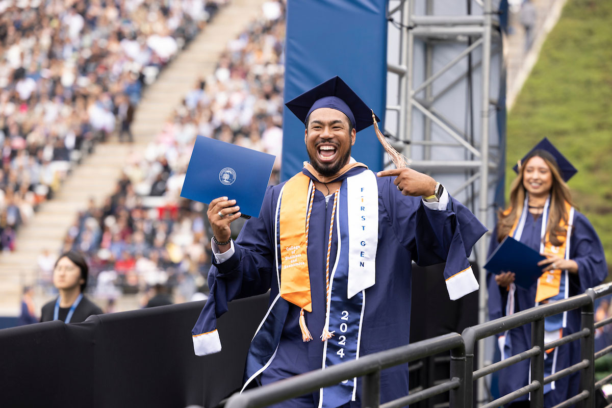 Man in graduation gown and cap celebrating his 'First Gen' college graduation with diploma